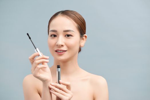 Young beautiful asian woman applying mascara on eyelashes