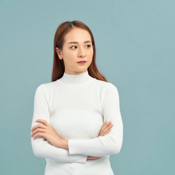 Photo of serious young lady with arms crossed dressed in blue dress standing and posing over white background.