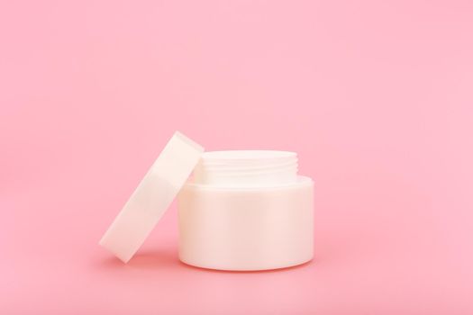 White glossy opened cosmetic jar against pink background. Close up of face cream, scrub or mask on simple background