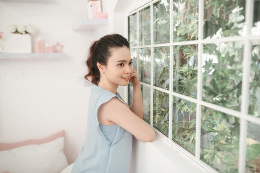 Happy cheerful young girl standing near a window at home