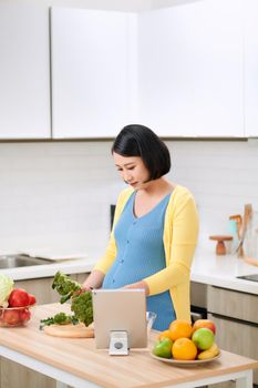 Pregnant woman cutting broccoli for fresh green salad, healthy nutrition for future mother