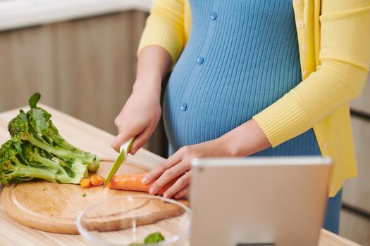 Beautiful smiling young pregnant woman preparing healthy food with lots of fruit and vegetables at home kitchen