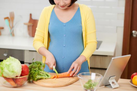 Beautiful smiling young pregnant woman preparing healthy food with lots of fruit and vegetables at home kitchen