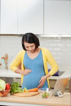 Young pregnant woman preparing healthy food with lots of vegetables at home kitchen