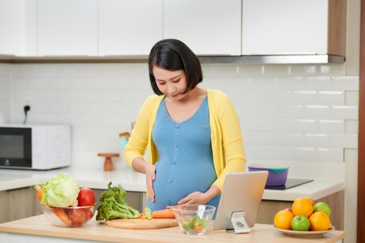 Pregnant woman in dress holds hands on belly on kitchen