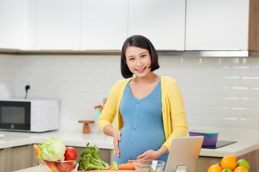 Young pregnant woman preparing healthy food with lots of vegetables at home kitchen