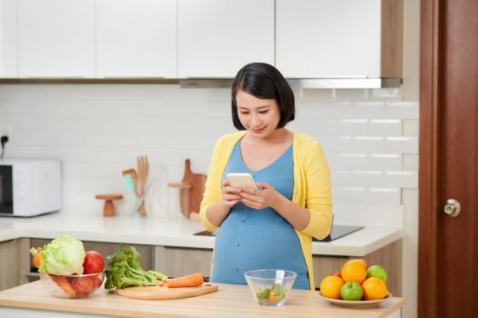 Pregnant woman in kitchen preparing food, using mobile phone