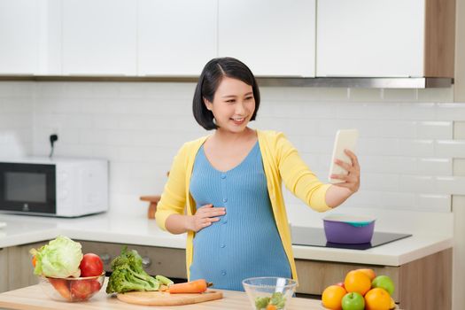 Pregnant woman in kitchen preparing food, using mobile phone