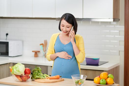 happy pregnant woman calling on smartphone and having breakfast at home kitchen