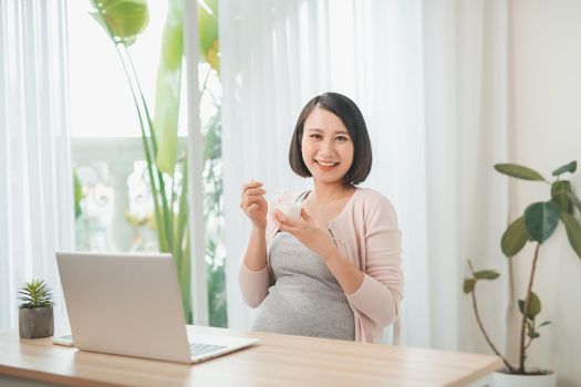 pregnancy, people and rest concept - close up of happy pregnant woman eating yogurt for breakfast at home