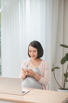 pregnant girl using laptop and cellphone in living room