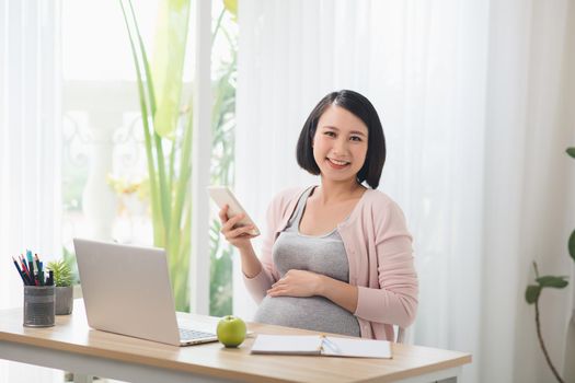 Asian Pregnant hard working, eatting and using the technology laptop together, with green apple for the breakfast