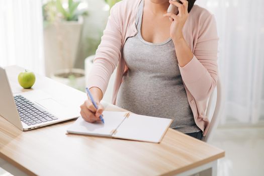 Cheerful asian pregnant woman talking on smart phone