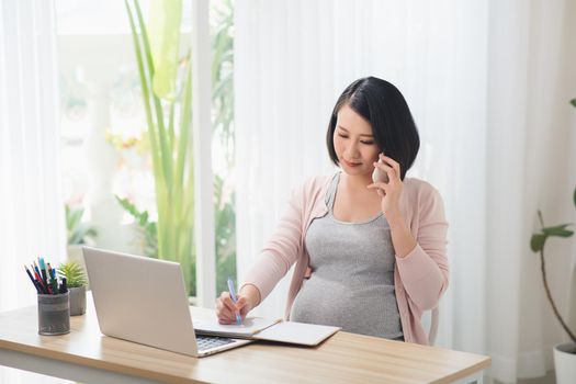 Cheerful asian pregnant woman talking on smart phone