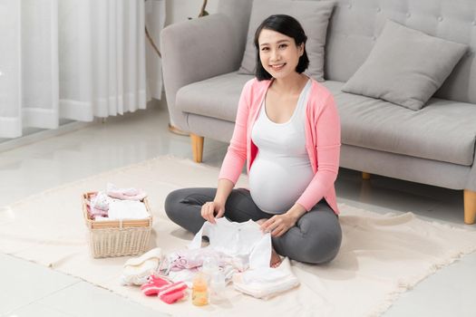 Pregnant woman with baby clothes at home, 