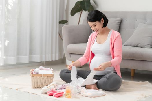 beautiful pregnant asian woman preparing baby clothes in basket