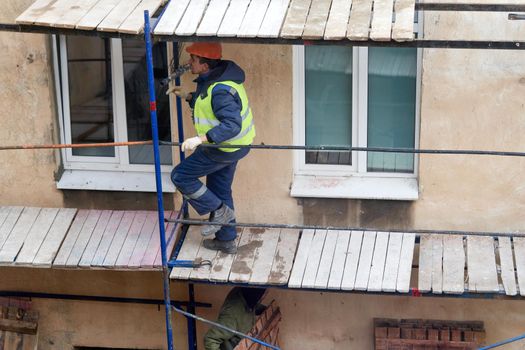 A builder installs wooden scaffolding to renovate an old house. Preparing to renovate the facade of an old house