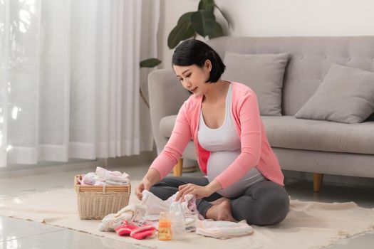 Cheerful pregnant preparing baby clothes and making to do list, getting ready for baby delivering