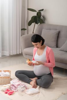 a pregnant woman at home on the floor checking list of baby clothes preparing for going to maternity hospital