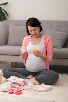 beautiful pregnant asian woman using pen writing list on notebook packing and preparing baby clothes in basket