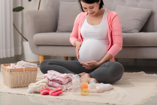 A happy pregnant woman checking a list of things for her unborn baby at home on the floor