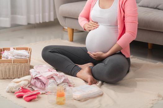 Beautiful pregnant asian woman packing and preparing baby clothes in basket for expectant new born baby