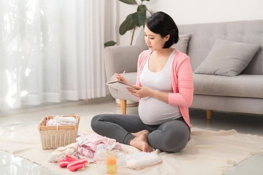 Pregnant woman with baby clothes at home, 