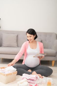 a pregnant woman at home on the floor checking list of baby clothes preparing for going to maternity hospital