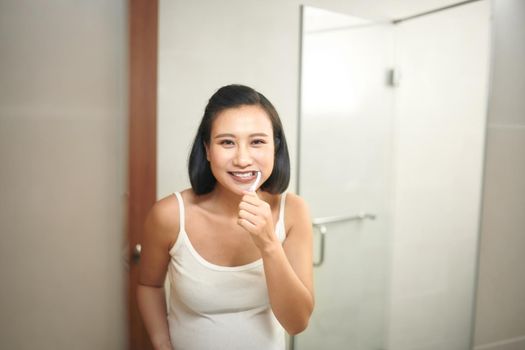 Portrait of young pregnant woman brushing teeth at bathroom