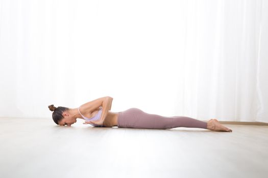 Portrait of gorgeous active sporty young woman practicing yoga in studio. Beautiful girl practice Bhujangasana, cobra yoga pose. Healthy active lifestyle, working out indoors in gym.