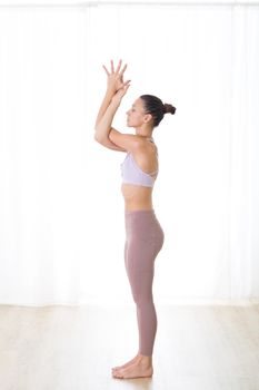 Portrait of gorgeous active sporty young woman practicing yoga in studio. Beautiful girl practice Garurasana, eagle yoga pose. Healthy active lifestyle, working out indoors in gym.
