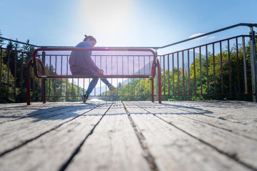 Young woman is sitting on bench, enjoying the view over a river