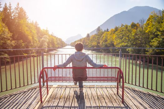 Young man is sitting on bench, enjoying the view over a river