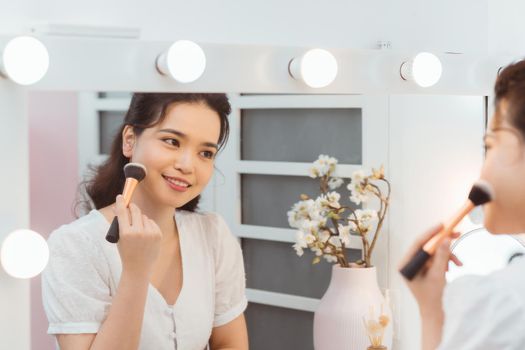 A beautiful young woman sitting at a makeup table and doing her makeup.