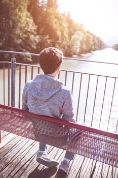 Young man is sitting on bench, enjoying the view over a river