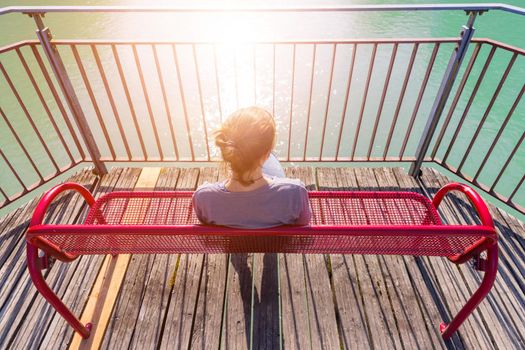 Young woman is sitting on bench, enjoying the view over a river