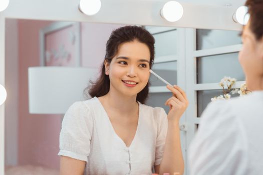 Amazing young woman doing her makeup in front of mirror.