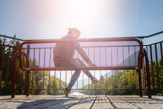 Young woman is sitting on bench, enjoying the view over a river
