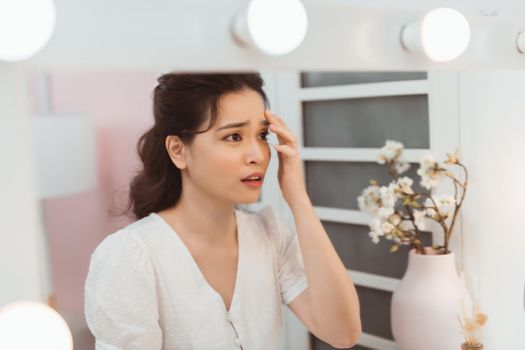 woman look mirrior feel upset and touch her face with acne problem