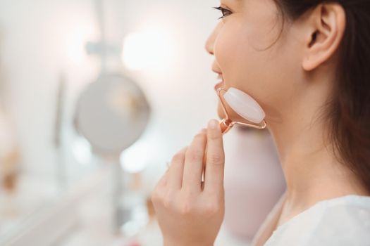 Woman massaging her face with rose quartz facial roller. Face lift, anti aging treatment concept. Copy space