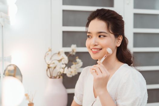 Woman using jade facial roller for face massage at home. 