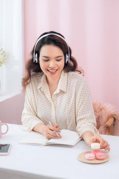 Beautiful young Asian woman listening to music and eating macarons.