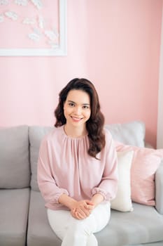 Asian woman smiling and relaxing on sofa at home.