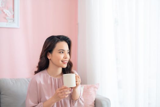 Attractive young Asian woman drinking coffee when sitting on sofa.