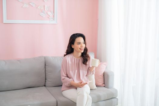 Beautiful young Asian woman drinking coffee when sitting on sofa