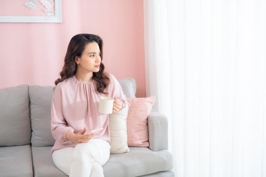 Beautiful young Asian woman drinking coffee when sitting on sofa