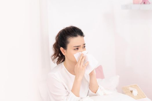 Sick woman with headache sitting under the blanket. Sick woman with seasonal infections, flu, allergy lying in bed