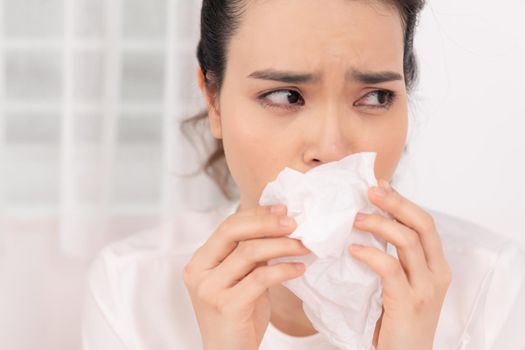 Sick woman covered with a blanket lying in bed with high fever and a flu, blowing her nose.