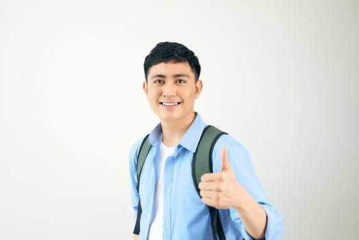 Portrait of a smiling male student with backpack showing thumbs up over white background