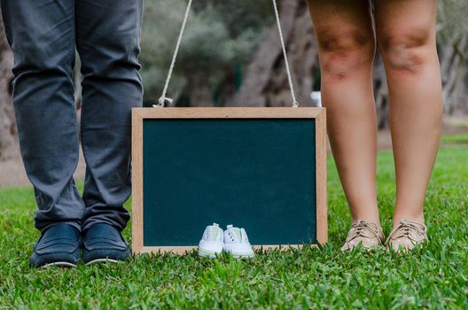 Feet of father and mother with baby shoes and a black slate, concept for the baby's welcome